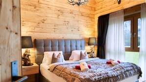A wooden-paneled bedroom with a large bed, two bedside lamps, and a view of the outdoors through a window. - Chalet Lessner - Pure Design & Tranquility (Leutasch)