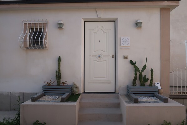A building with a white door, a small window with metal bars, and two planters with cacti.