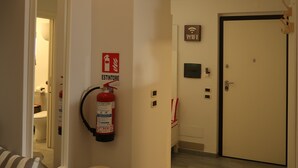 Ein Flur mit einer weißen Vase, einem Feuerlöscher, einem WLAN-Symbol und einer Tür.