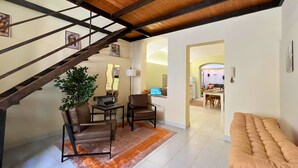A spacious living area with a wooden ceiling, a staircase, a sofa, a coffee table, and a dining area visible in the background. - NEW Central Stylish Flat/Private Patio/2min Subway (Catania)