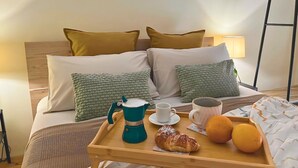 A neatly made bed with a wooden headboard, two pillows, a bedside lamp, and a tray with a croissant, two oranges, and two cups. - NEW Central Stylish Flat/Private Patio/2min Subway (Catania)