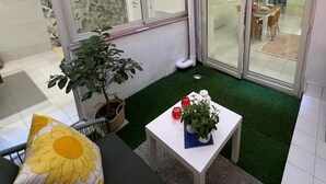 A small, enclosed patio area with a glass door leading to a dining area, a potted plant, and a small table with a flower vase. - NEW Central Stylish Flat/Private Patio/2min Subway (Catania)