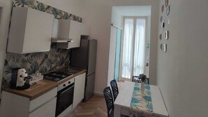A compact kitchen with a modern stove, a refrigerator, and a dining area with a table and chairs. - Modern vacation home for couples and families - central area (Napoli)