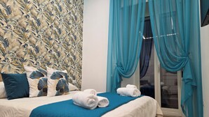 A hotel room with a floral wallpaper, a bed with blue bedding, and a view through a glass door. - Modern vacation home for couples and families - central area (Napoli)