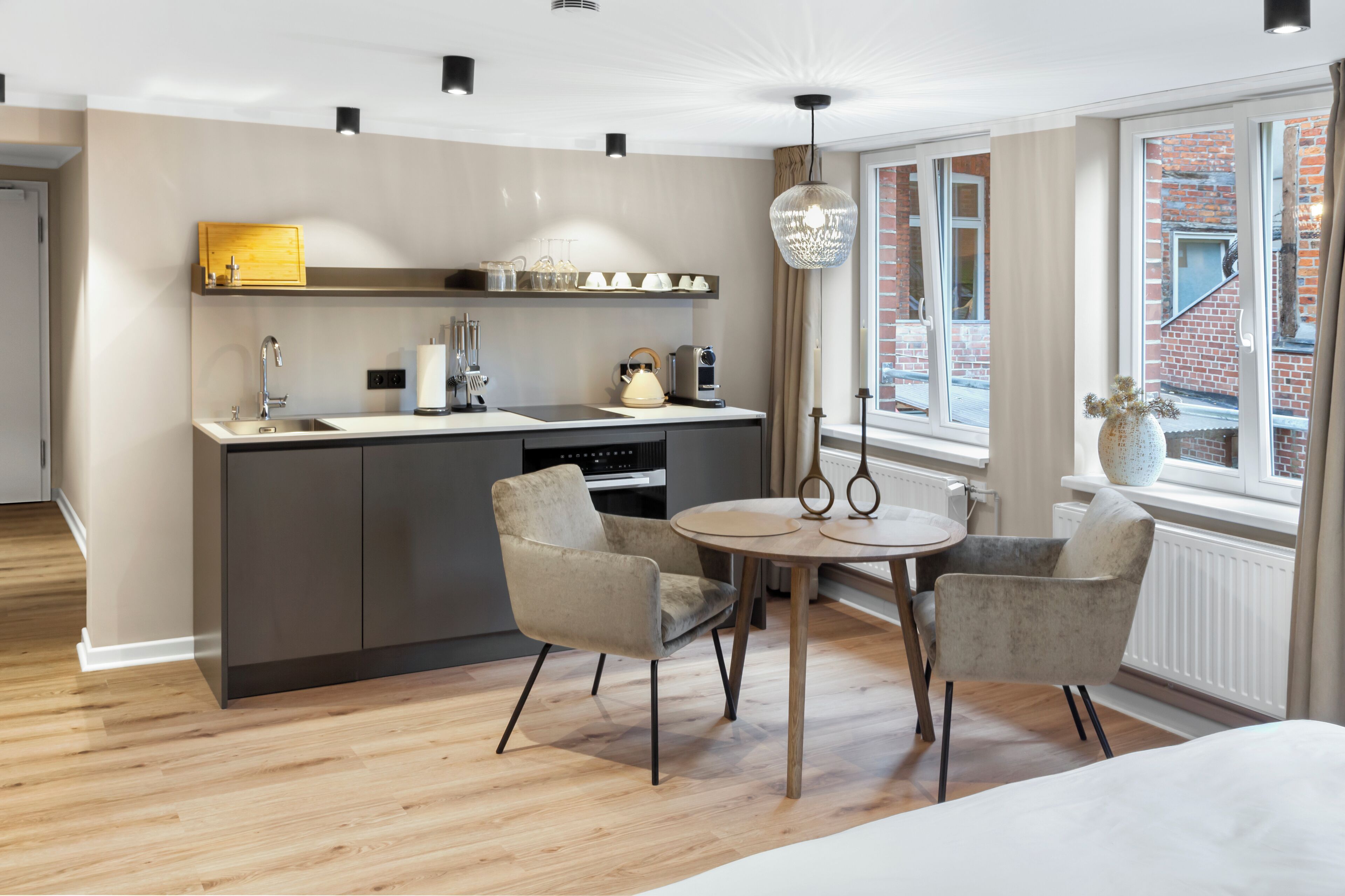 A modern kitchen with a central island, a dining area with two chairs, and a large window with a view of a brick building.