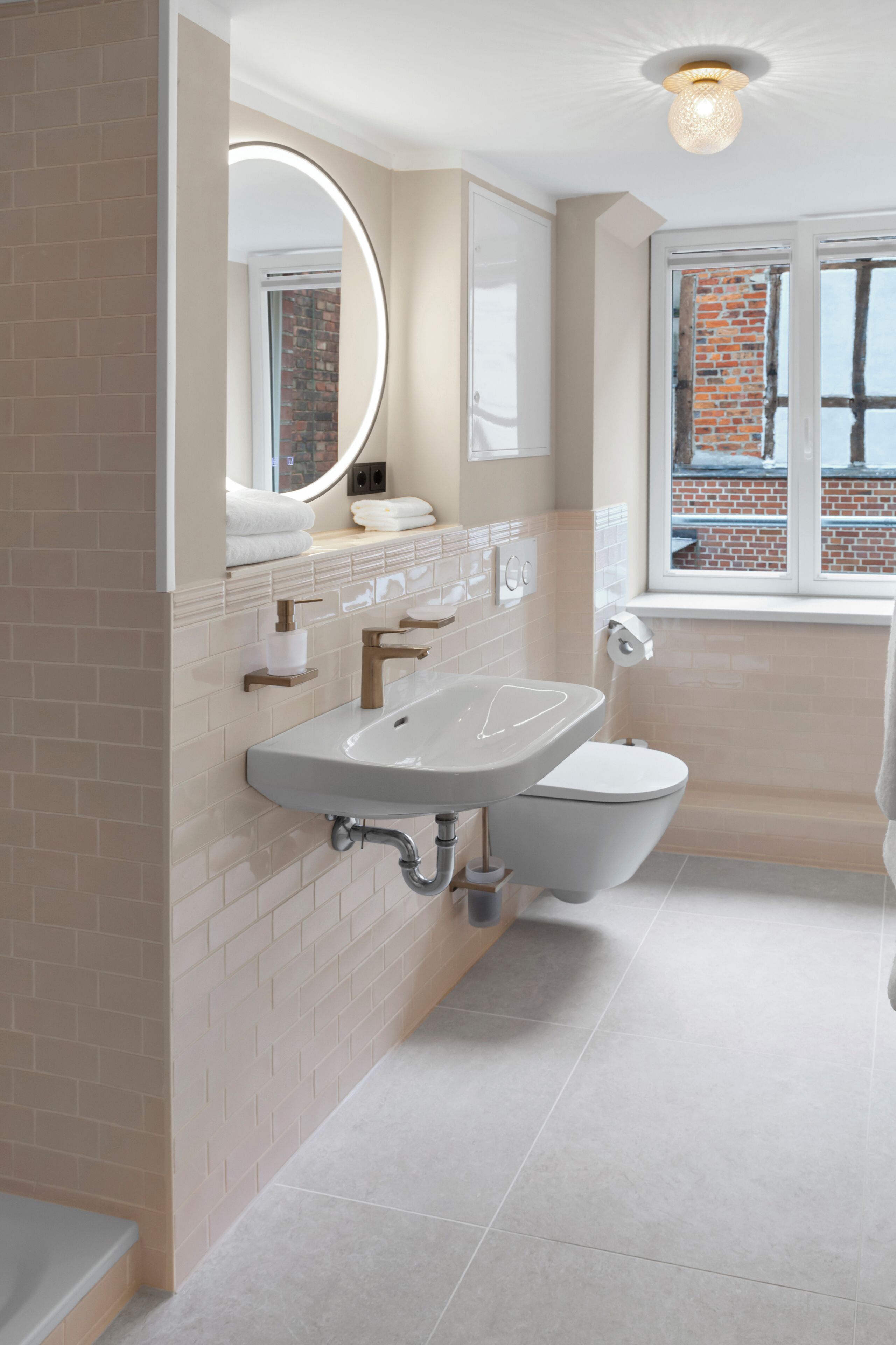 A modern bathroom with a large sink, toilet, and a window with a view of a brick building.