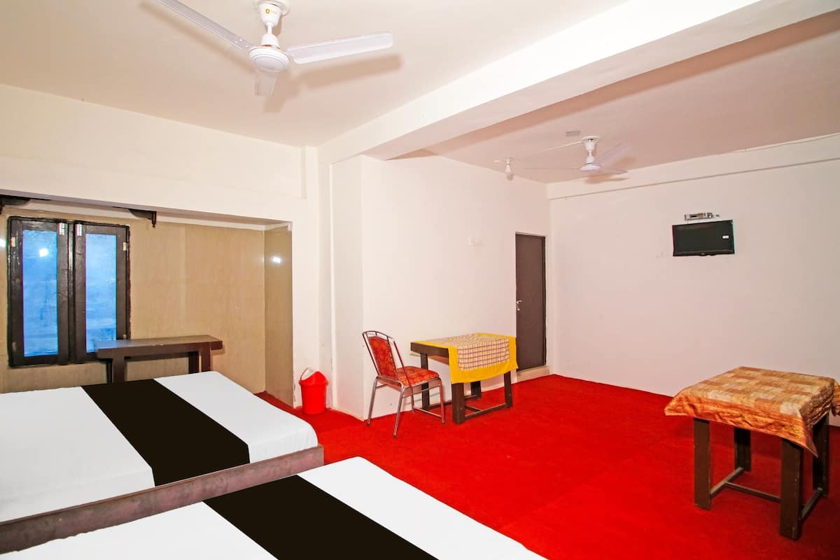 A hotel room with two beds, a red carpet, a desk with a chair, and two ceiling fans.