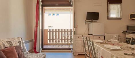 Una habitación acogedora con sofá, una mesa de comedor para dos, televisión y refrigerador.