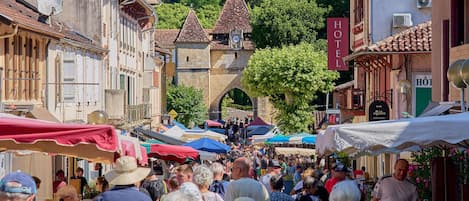 Un marché animé en plein air, avec de nombreux étals, et un bâtiment historique doté d’une tour de l’horloge en arrière-plan.