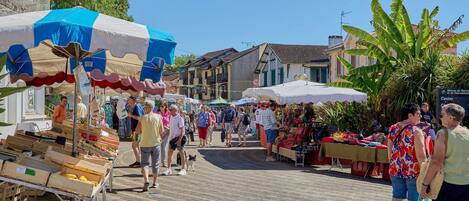 A bustling outdoor market with vendors and shoppers, wooden stalls, and a clear blue sky.