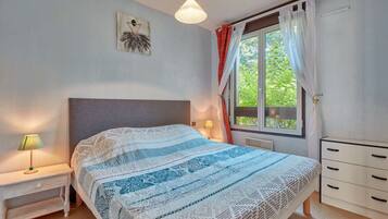 Une chambre à coucher comprenant un lit, des tables de chevet, une commode, une fenêtre avec des rideaux et un tableau accroché au mur.
