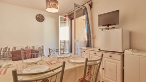 A dining area with a table set for four, a clock on the wall, and a television mounted above a white cabinet.