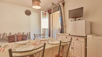 Un coin repas avec une table dressée pour quatre personnes, une horloge au mur et un téléviseur fixé au-dessus d’un meuble blanc.