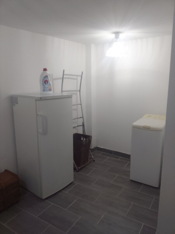 Een kleine wasruimte met een wasmachine, een droger en een metalen rek.