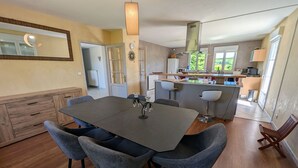 A modern kitchen with a central island, a dining area with a dark table and grey chairs, and a visible clock on the wall.