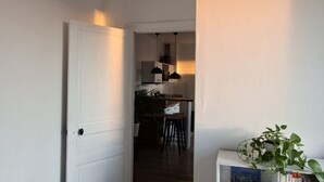 A hallway leading to a dining area with a table and chairs, a hanging light fixture, and a potted plant.