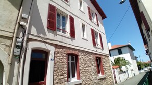 A two-story building with stone facade, red shutters, and a clear sky.