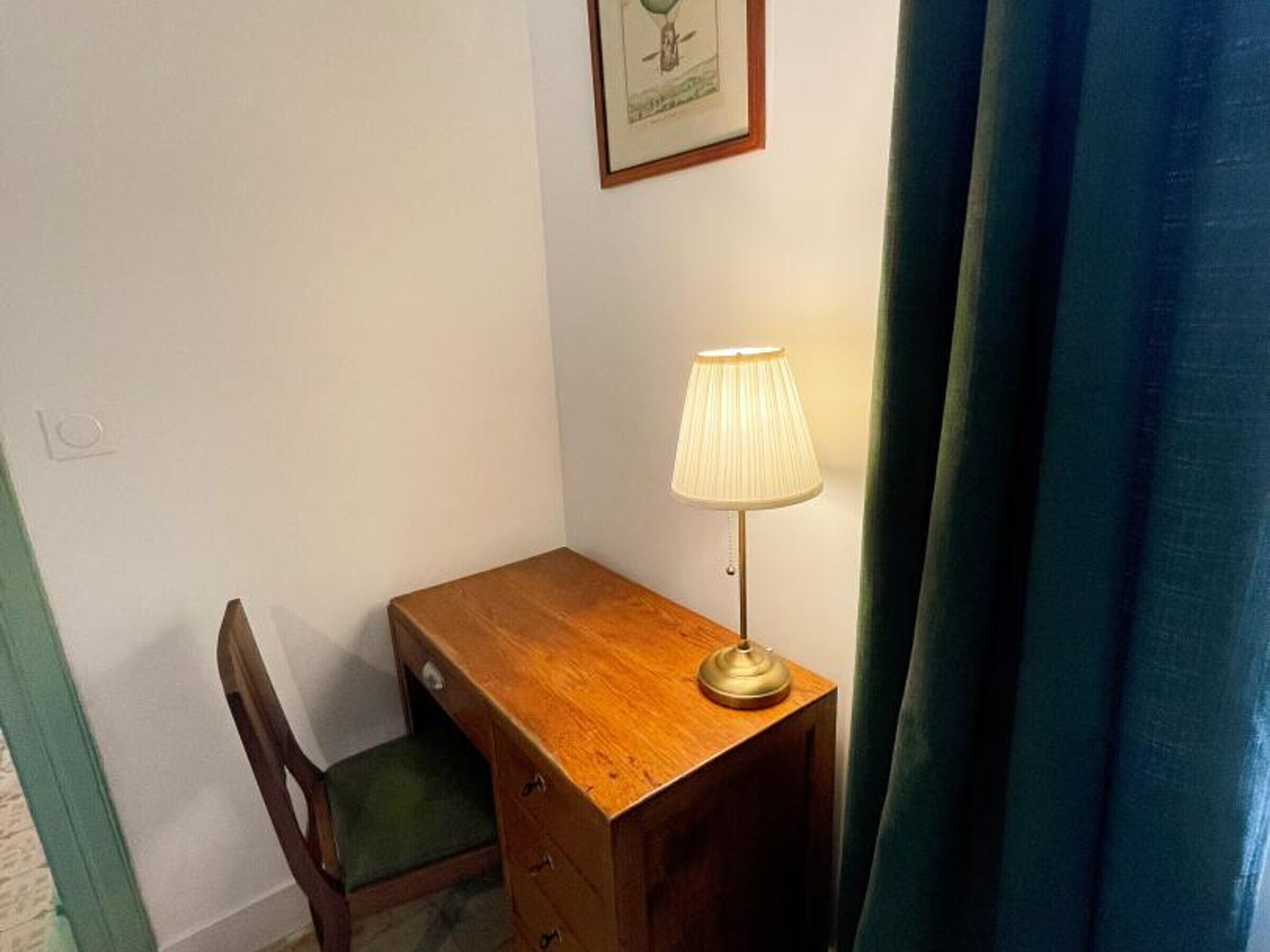 Una piccola scrivania in legno con una lampada, una sedia e un quadro appeso al muro.
