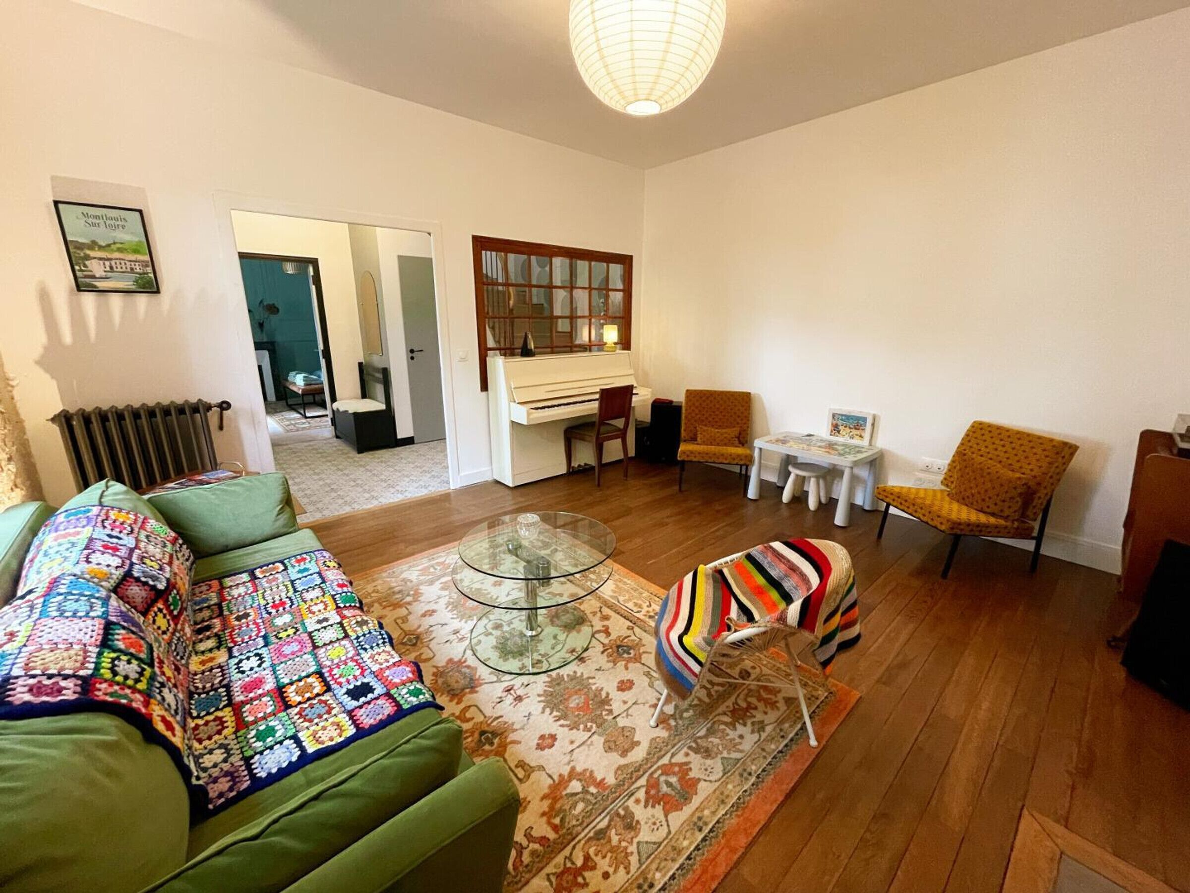 A living room with a green sofa, a piano, a small table, and a colorful blanket on the floor.