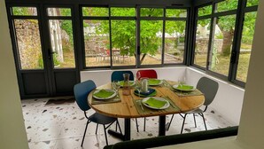 Un espace repas comprenant une table ronde, des chaises et une vue sur un jardin, grâce à de grandes fenêtres.