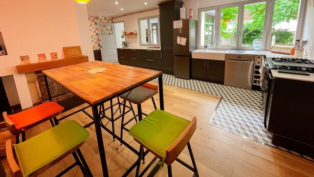 Une cuisine moderne avec une table en bois, deux chaises vertes, un réfrigérateur noir et une fenêtre donnant sur un paysage verdoyant.