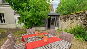 Une table à manger en bois, conçue pour l’extérieur, avec des chaises en osier, agrémentée de nappes rouges et de porte-bougies orange.