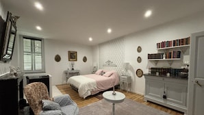 Une chambre à coucher comprenant un lit, des tables de chevet, une chaise, une petite table ronde, une bibliothèque et un radiateur.