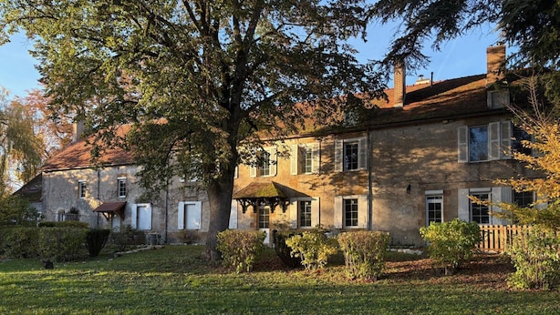 Un bâtiment en pierre doté de nombreuses fenêtres et d’un grand arbre qui se trouve devant.