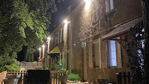 Un bâtiment rustique doté d’une terrasse en bois et d’un espace extérieur aménagé pour s’asseoir, le tout éclairé par des lampadaires.