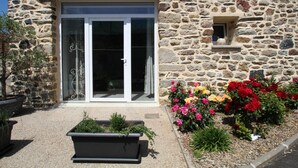 A stone building with a large glass door and windows, surrounded by a gravel driveway and potted plants. - Bright house with terrace and private garden near the beach (Bretteville)