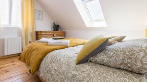 A bedroom with a sloped ceiling, a skylight, a wooden dresser, a bed with floral bedding, and a window with yellow curtains. - Bright house with terrace and private garden near the beach (Bretteville)