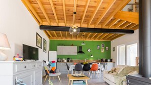 A cozy living room with a fireplace, a dining area with chairs and a table, a kitchen with cabinets and a green wall, and a TV on a white cabinet. - Bright house with terrace and private garden near the beach (Bretteville)