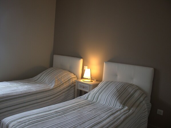 Two twin beds with striped bedding, a bedside table with a lamp, and a plain wall.