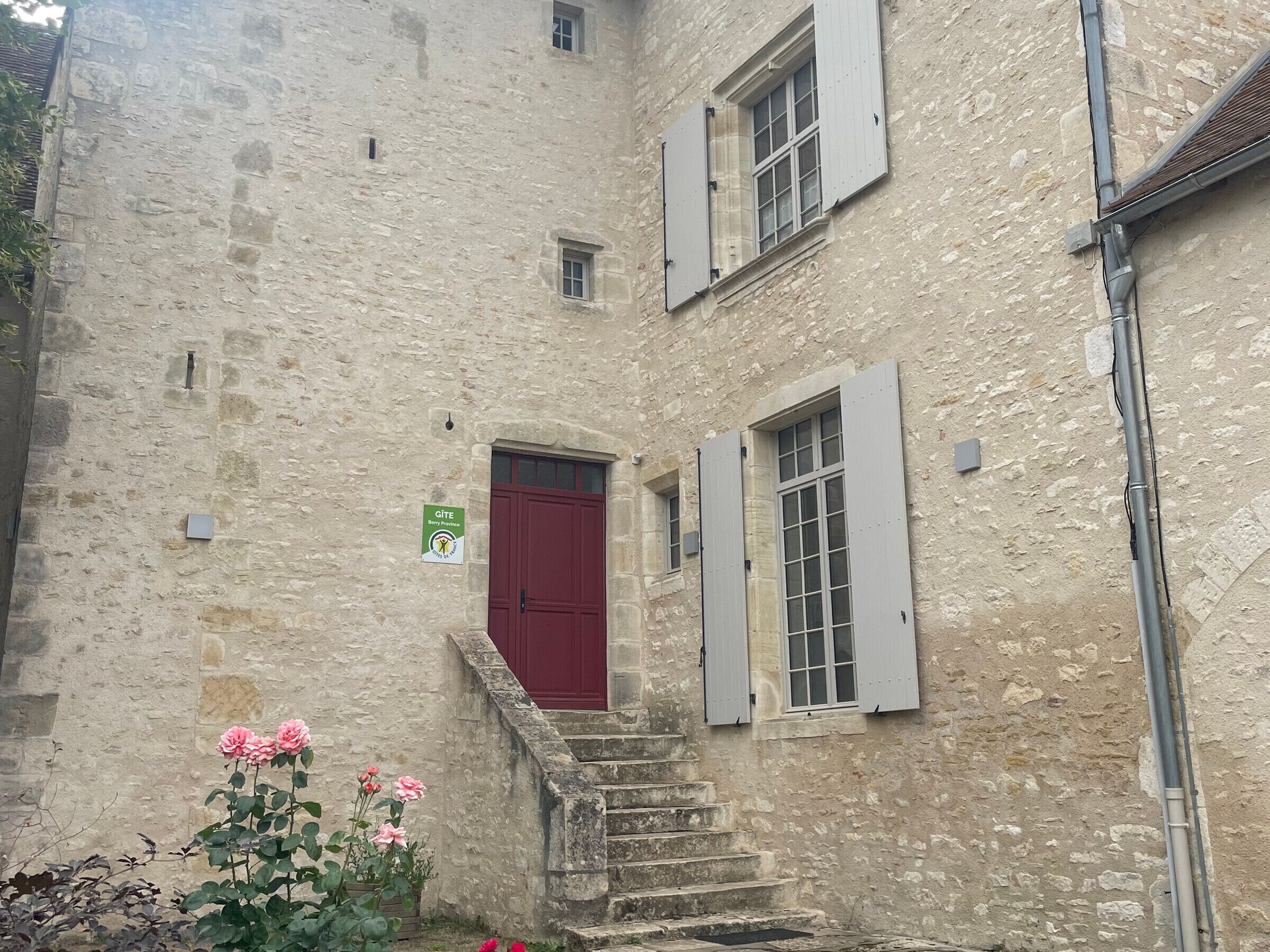 A stone building with a red door, a small window, and a sign indicating a gîte.
