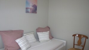 Ein Bett mit Kissen, ein Holzstuhl und eine Wand mit einem Gemälde.