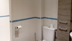 Ein Badezimmer mit weißen Fliesen, einem Holzschrank und einer Toilette.