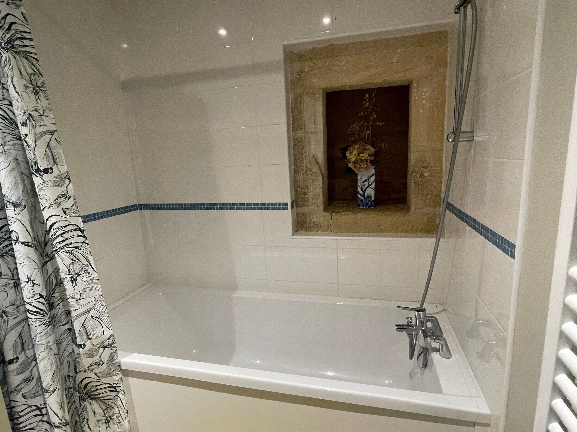 Une salle de bain avec une baignoire, une douche et une petite fenêtre agrémentée d’un vase.