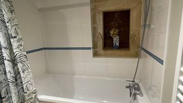 A bathroom with a bathtub, a shower, and a small window with a vase.