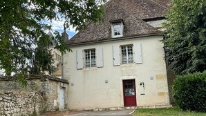 Un edificio de dos pisos con puerta roja, contraventanas blancas y una pared de piedra en un lateral.
