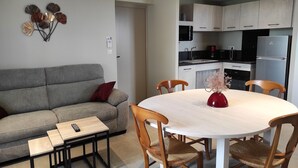 Una sala moderna con un sofá gris, una mesa de comedor de madera con sillas, una pequeña mesa de centro y un elemento decorativo en la pared.