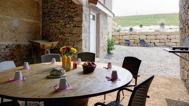 An outdoor dining area with a stone wall, wooden table, wicker chairs, and a view of the countryside. - Family cottage with fiber, in the peaceful Monts du Lyonnais (Panissières)