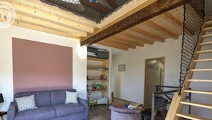 A cozy living room with a grey sofa, a small ottoman, and a wooden staircase. - Family cottage with fiber, in the peaceful Monts du Lyonnais (Panissières)