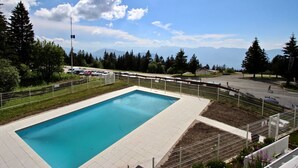 Una piscina rettangolare con bordo piastrellato, circondata da una recinzione, con uno sfondo di alberi e montagne.
