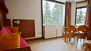 Una stanza con un letto di legno, un tavolo da pranzo con sedie e vista sugli alberi attraverso ampie finestre.
