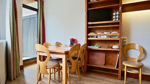 Zona pranzo con tavolo e sedie in legno, una macchina da caffè e un televisore su uno scaffale.