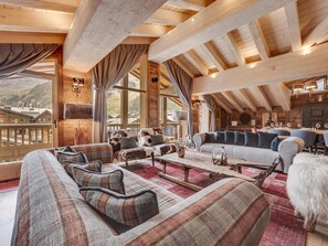 A cozy, wooden interior with a high ceiling, a seating area with sofas and a dining table, and a view of the mountains. - Luxury Penthouse in Val-d'Isère with Fireplace and Parking (Val-d'Isère)