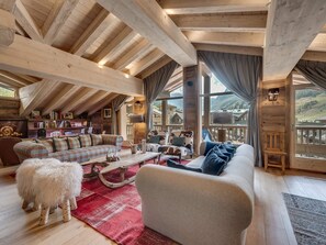 A cozy loft-style living room with a high ceiling, wooden beams, a fireplace, and a view of a mountainous landscape.
