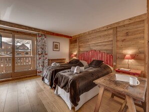 A room with two beds, a wooden headboard, a table with a lamp, and a view of buildings outside. - Luxury Penthouse in Val-d'Isère with Fireplace and Parking (Val-d'Isère)