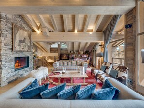 A cozy living room with a stone fireplace, wooden beams, a sofa with blue cushions, and a dog.