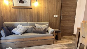 Un salón con suelo de madera, un sofá, una mesita con una revista y una puerta de madera.